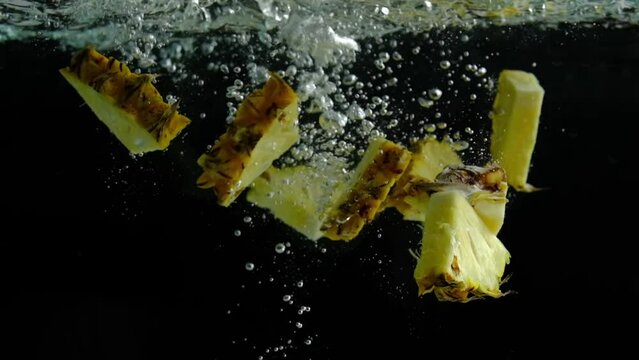 Slow motion of sliced pineapple dropped down into water in black background 