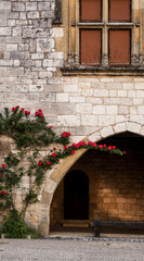 Red roses grow on beautiful Romanesque architecture in a small French village in the south of France at Monpazier, next to the Chateaux de Biron