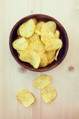 Potato chips in bowl on a wooden background, top view. Fast food. Crispy potato on table wooden background. American tradition.