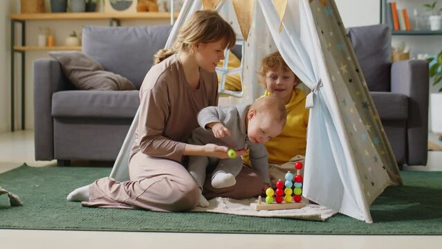 Mother and two little kids playing with developmental toy in teepee tent at home