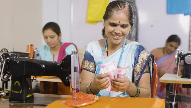 happy garment worker or small business owner counting money infront of sawing machine - concept of earnings, profit, finance and banking.
