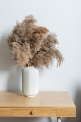 Close up of work table with a composition of dried pampas grass in a cylindrical ceramic vase as a home decoration.
