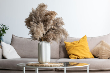 Minimalist modern interior with a composition of dried pampas grass in a cylindrical ceramic vase in the foreground as a home decoration.
