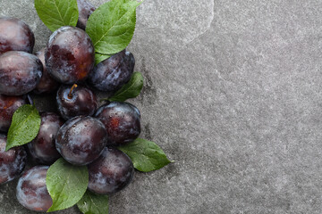 Pile of fresh purple plums with drops on stone table, top view.