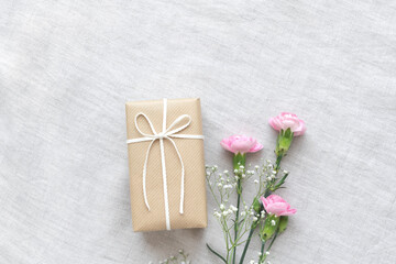 明るいグレーの布の上のプレゼントとピンクのカーネーションとかすみ草
