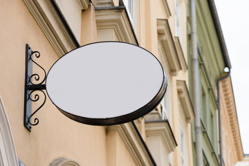 Blank metal oval store signboard on street hanging mounted on the wall. Empty plastic sign board mockup.