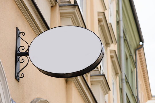 Blank Metal Oval Store Signboard On Street Hanging Mounted On The Wall. Empty Plastic Sign Board Mockup.