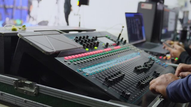 Selective focus of male sound engineer's hand sliding and pushing the buttons on the professional audio mixer console, working controlling on sound system in an editing zone in a filming studio.