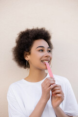 pleased african american young woman eating sweet jelly bubble tape on white