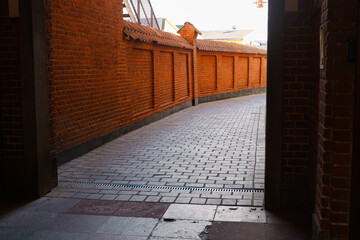 Narrow road surrounded by red brick walls. Narrow alley between two red brick walls in perspective.