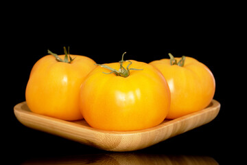 Three yellow juicy tomatoes on a bamboo tray, macro, isolated on a black background.