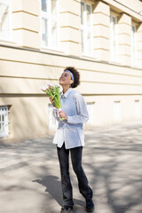 cheerful african american woman holding bouquet of tulips and walking on street