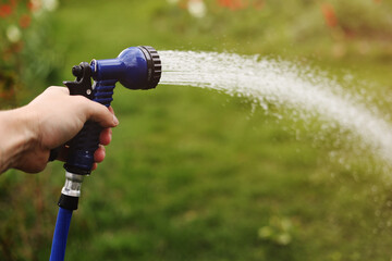 Watering green garden with outdoor hose. hand with hose sprinkle watering plants in the garden. watering lawn or plants on backyard. gardener man with sprinkler in garden