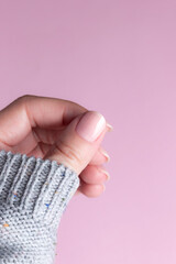 Female hand in gray knitted sweater with beautiful natural manicure - pink nude nails on pink background. Nail care concept