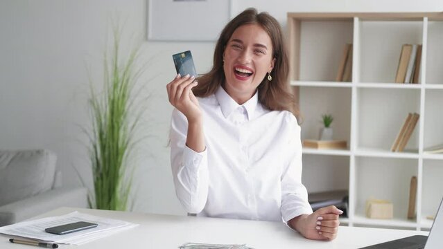 Online payments. Hesitating woman. Money keep. Puzzled pretty lady choosing credit card in spite cash dollars to use sitting desk in light room interior.