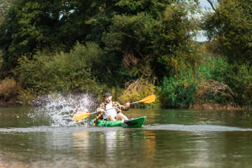 Happy bearded man in shirt and cap kayaking at the river with splashes. The concept of the World Tourism Day and watersport