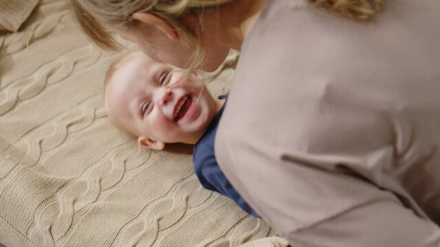 High angle shot of adorable toddler boy lying on sofa and smiling while cheerful mother playing and rubbing noses with him
