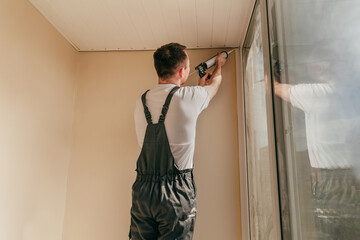 Young man wearing overalls sealing cracks between window and trim