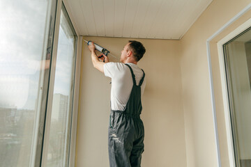 Young man wearing overalls sealing cracks between window and trim