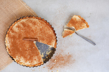 Traditional South African milk tart freshly baked and in tin. Mottled grey and rustic surface with...