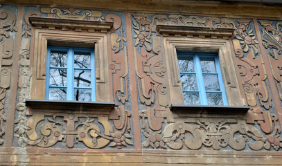 Zdjęcie architektury przedstawiające dwa okna w kamienicy pokrytej płaskorzeźbą