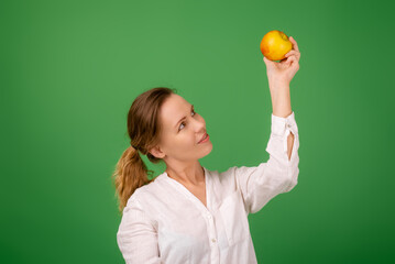 A good-looking woman of forty in a white shirt on a green background smiles and holds a fresh apple in her hands. Healthy eating, vegetarianism, healthy appearance concept.