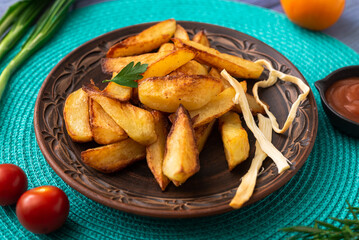 Fried potatoes in large pieces on a plate on a turquoise napkin on the table with different vegetables.