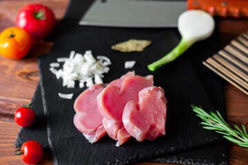 Chunks of sliced raw turkey meat, chopped onions, on a black slate background.