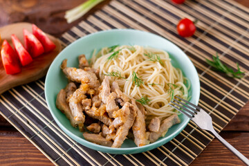 Fried meat and spaghetti on a plate on a wooden background with tomatoes and herbs.