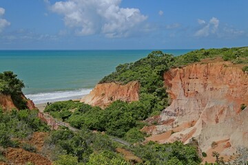 Orange cliff in the middle of green vegetation. In front the sea with small white waves.  horizon  with clam sea.
