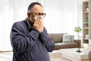 Man blowing nose with a paper tissue at home in a living room