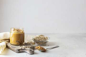 Sunflower seed oil in a transparent jar on a wooden board. Seeds in a glass vase in the background. Spoon with butter on the table. Light background, space for text