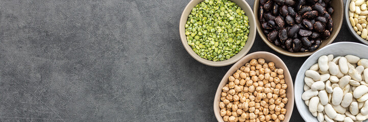 Banner of different types of legumes in bowls, green peas and chickpeas , colored beans and maash and peanuts, top view, copy space