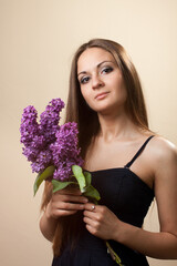 Beautiful young girl weared in black dress with a bouquet of lilac.