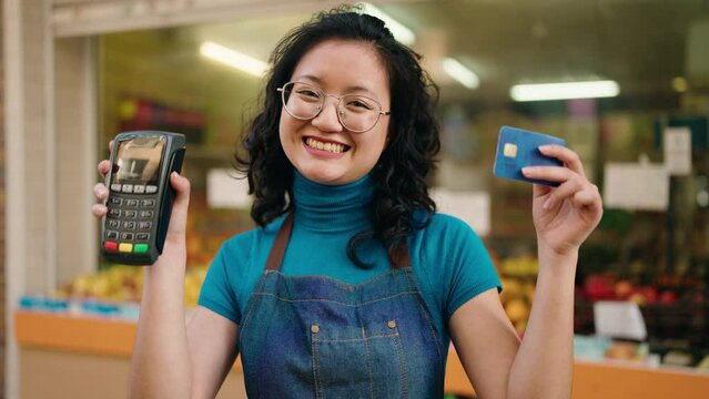 Young chinese woman employee holding data phone and credit card at fruit store