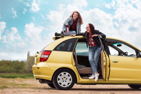 Happy mother and her teen daughter funny posing by a yellow car. Copy space. The concept of freedom and car trip