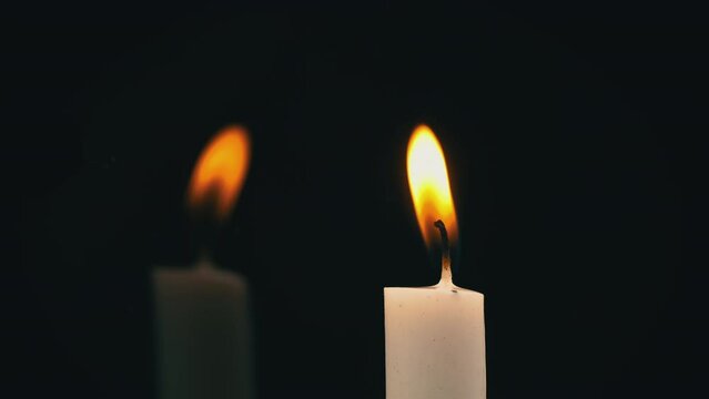 White paraffin candle with yellow tints burns on black background in reflection. One wax candle burns motionless and emits fire.