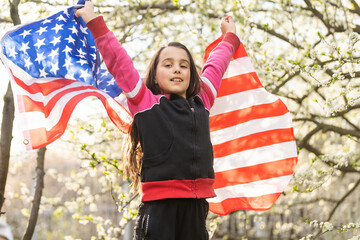 Happy adorable little girl smiling and waving American flag. Patriotic holiday. Happy kid, cute little child girl with American flag. USA celebrate 4th of July. Independence Day concept.