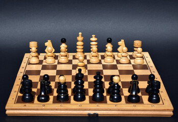 Wooden chess board with chess pieces on and black background.