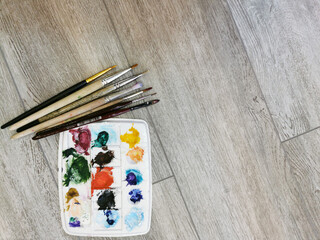 Palette with samples of multi-colored gouache paints and brushes after painting. Close-up on a...