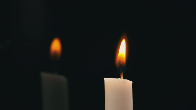 White paraffin candle is lit with a match on a black background in reflection. One wax candle burns motionless and emits fire.