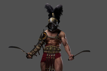 Studio shot of antique gladiator with muscular build and two swords isolated on gray background.