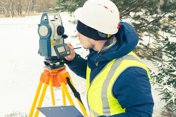 cadastral works with an electronic total station, a male cadastral engineer performs measurements with a tool for geodetic measurements on the ground selective focusing, tinting. - obrazy, fototapety, plakaty