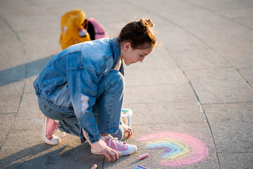 A cute girl draws a rainbow with crayons on the street. Creation. Kids. Street.