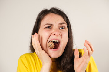 A woman gnaws on a walnut, opening her mouth wide, breaking a tooth or dislocating the temporomandibular joint, her jaw has moved away.