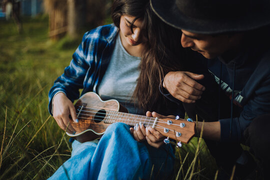 Mujer aprendiendo a tocar Ukulele o guitarra al aire libre. Concepto de educaci&oacute;n, m&uacute;sica y personas.