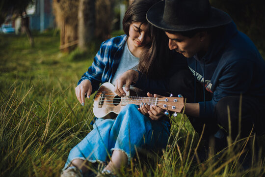 Mujer aprendiendo a tocar Ukulele o guitarra al aire libre. Concepto de educaci&oacute;n, m&uacute;sica y personas.