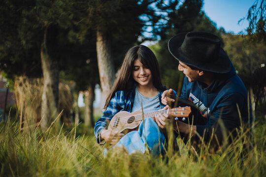 Mujer aprendiendo a tocar Ukulele o guitarra al aire libre. Concepto de educaci&oacute;n, m&uacute;sica y personas.