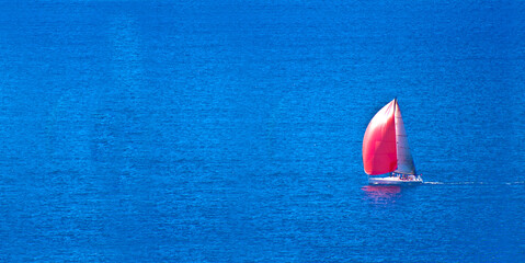 Sail boat with red sail on blue waters