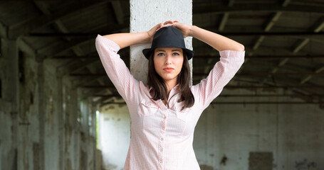 Young woman wearing hat, shirt, and jeans standing in abandoned building